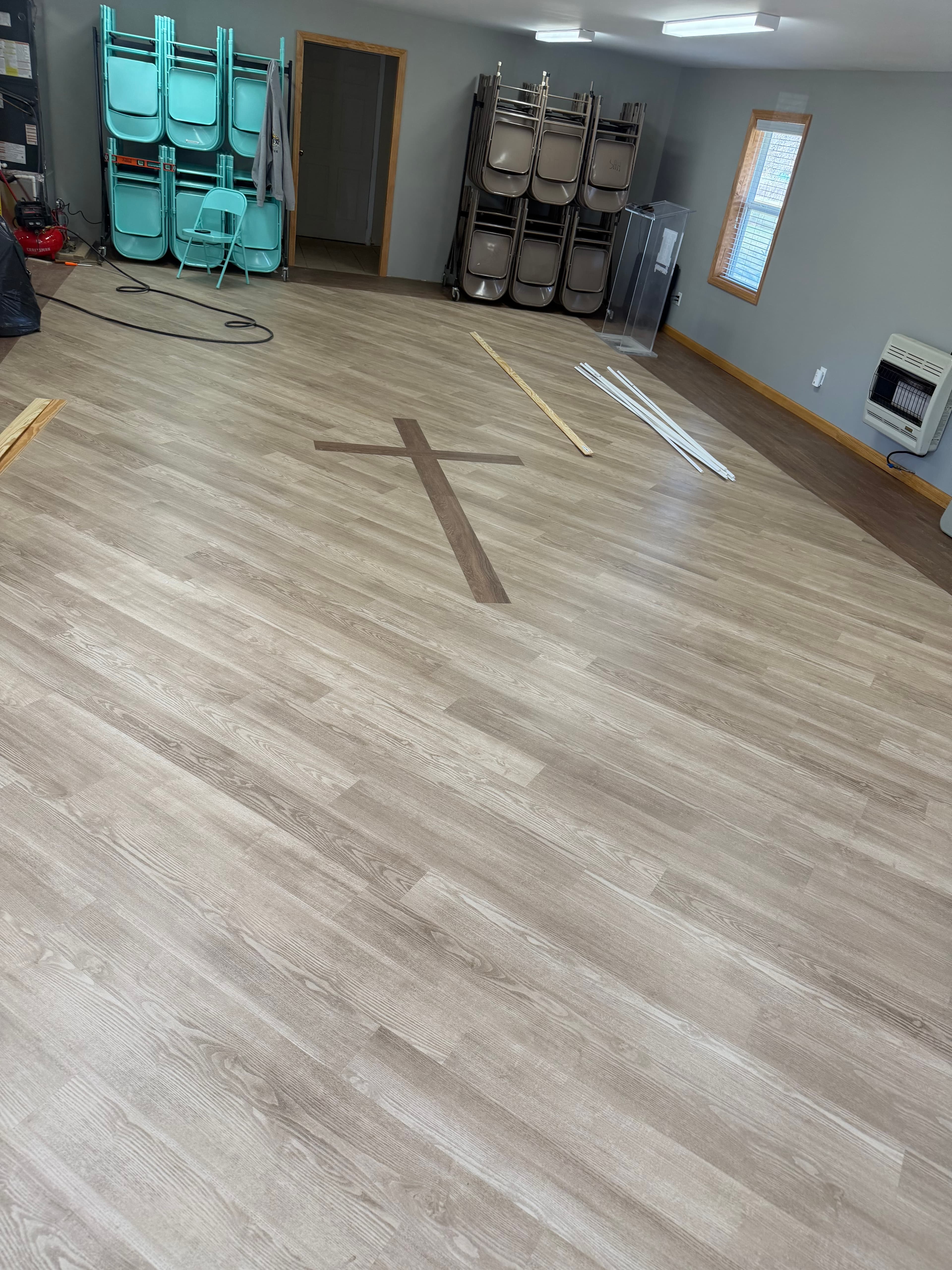 Light wood flooring featuring a dark cross inlay and stacks of folding chairs along walls.