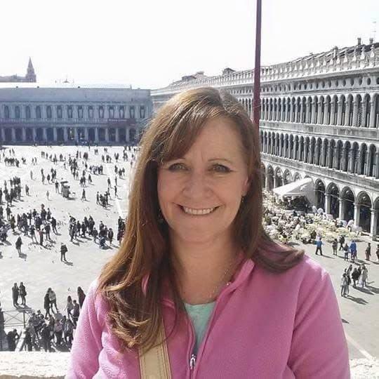 Smiling woman in a pink jacket posing at St. Mark's Square in Venice, Italy.